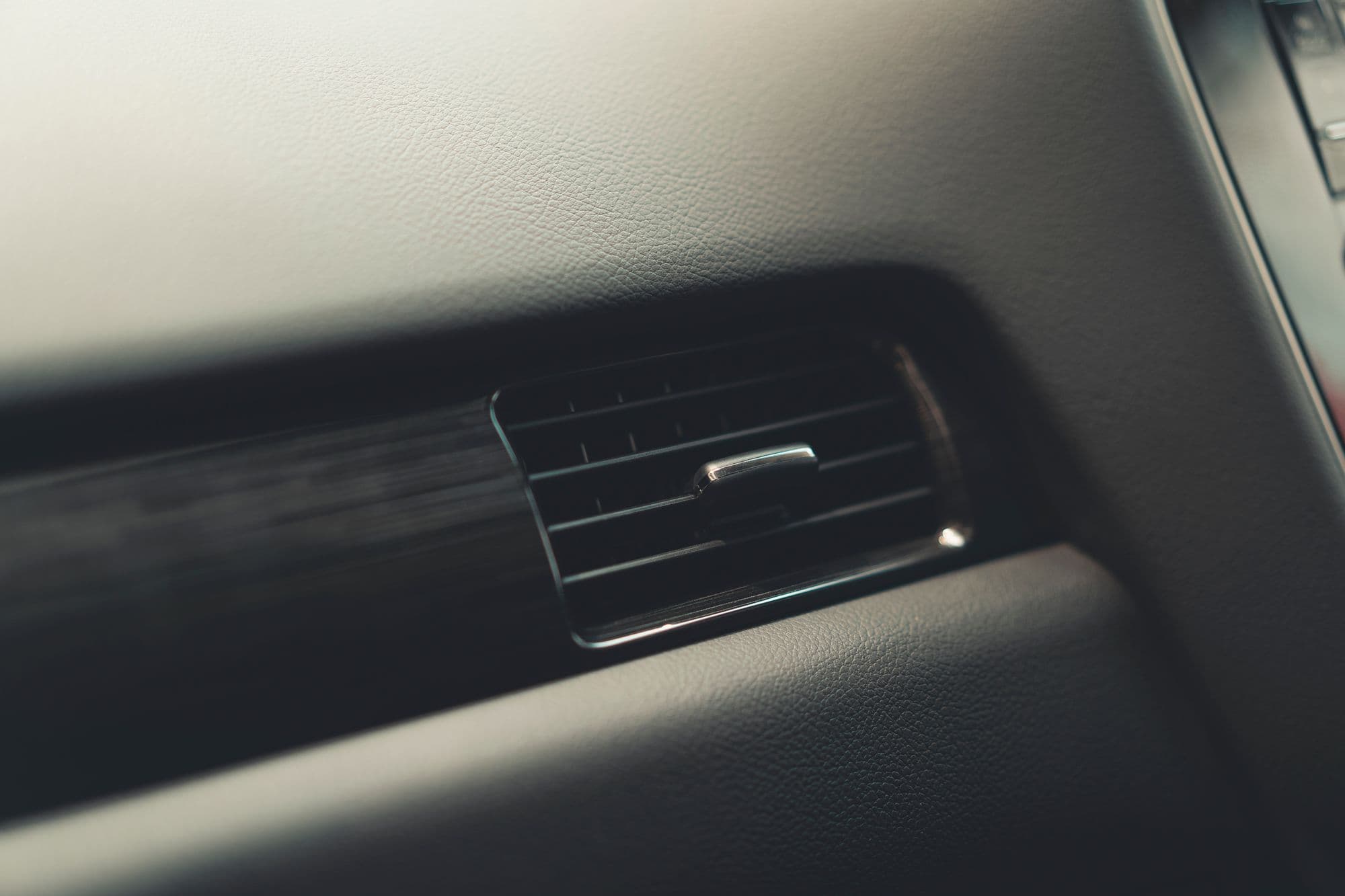 Détail d’un tableau de bord de voiture : une grille d’aération à réglette chromée entre un revêtement grainé et un insert sombre.